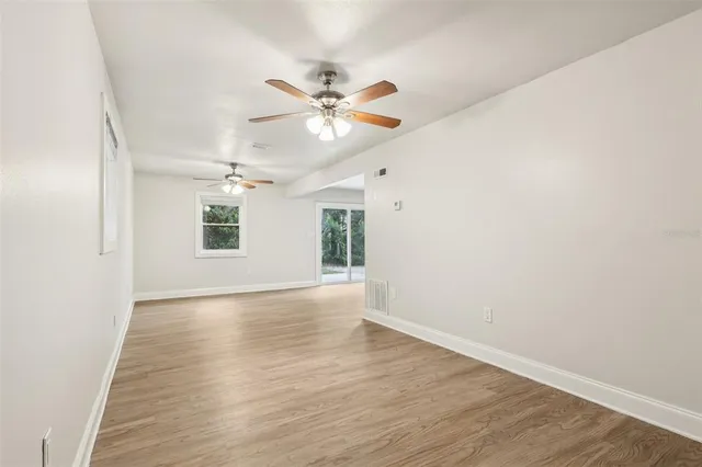 an empty room with wooden floor fan and windows