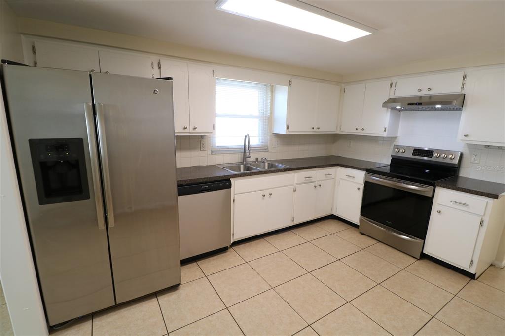 7825 Birchwood Drive Port Richey, FL 34668 - Photo 5 of 43 a kitchen with a sink a refrigerator a window and white cabinets