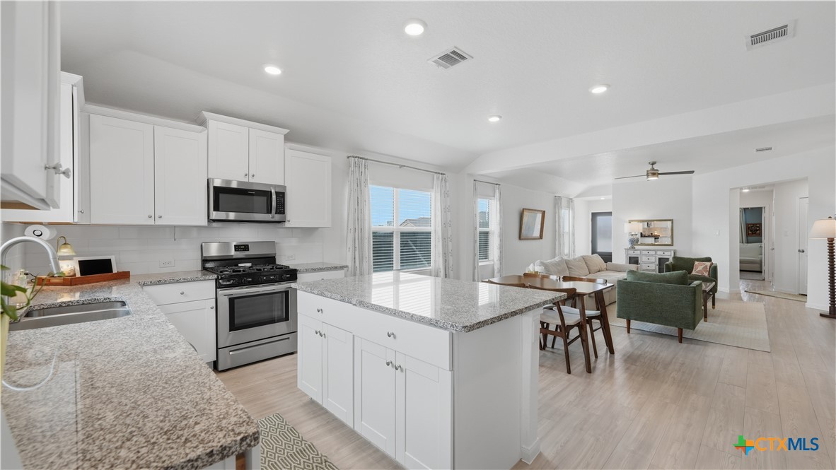 1949 Redstart New Braunfels, TX 78130 - Photo 13 of 32 a kitchen with stainless steel appliances granite countertop a stove top oven a sink a dining table and chairs with white cabinets