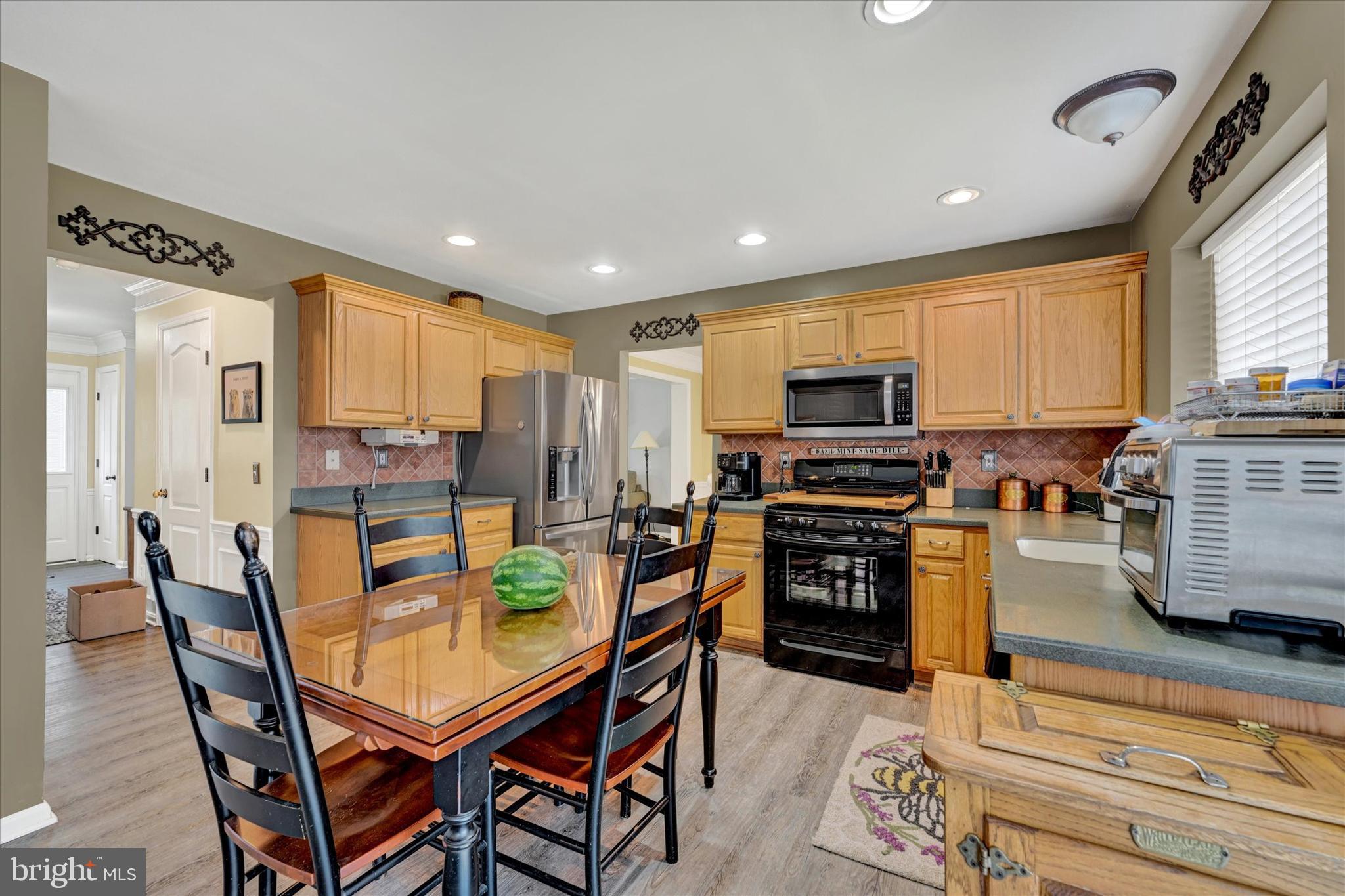 4642 Bucks School House Road Rosedale, MD 21237 - Photo 12 of 33 a kitchen with stainless steel appliances granite countertop a stove top oven a sink dishwasher a dining table and chairs with wooden floor