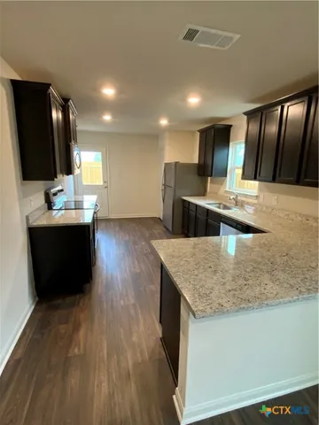 a kitchen with stainless steel appliances granite countertop a sink dishwasher a stove and a refrigerator with wooden floor