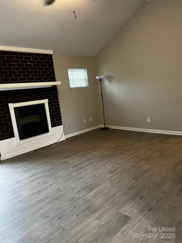 a view of an empty room with wooden floor kitchen view and a fireplace