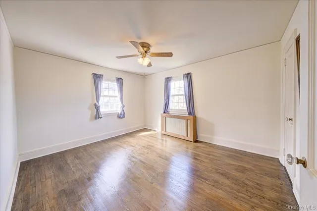 an empty room with wooden floor chandelier fan and windows