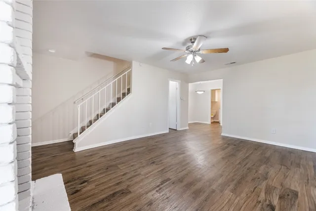 a view of an empty room with wooden floor and a ceiling fan