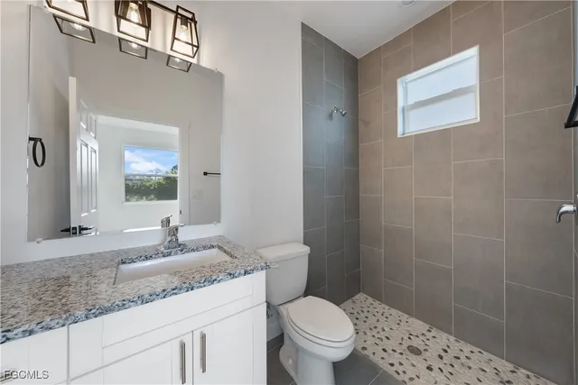 a bathroom with a granite countertop toilet a sink a mirror a window and vanity