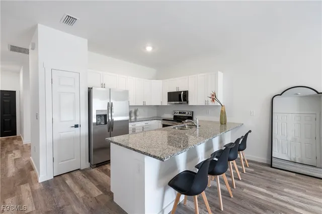 a kitchen with stainless steel appliances granite countertop a sink a stove a refrigerator and island with wooden floor