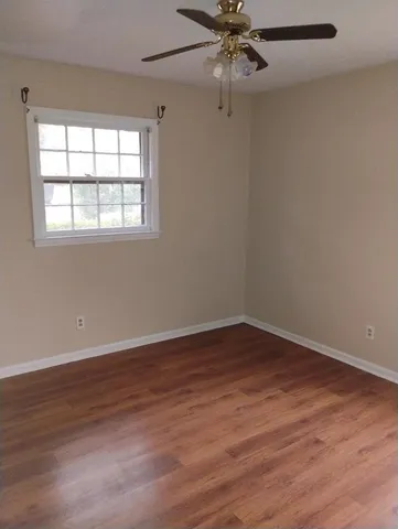 an empty room with wooden floor fan and windows