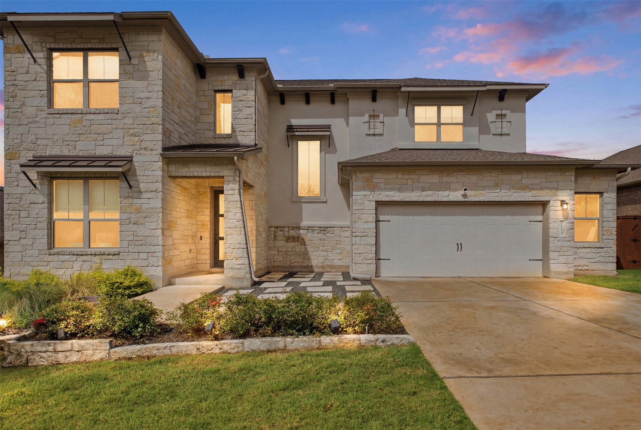 A striking modern facade features a blend of stone and stucco, illuminated by soft evening lights.
