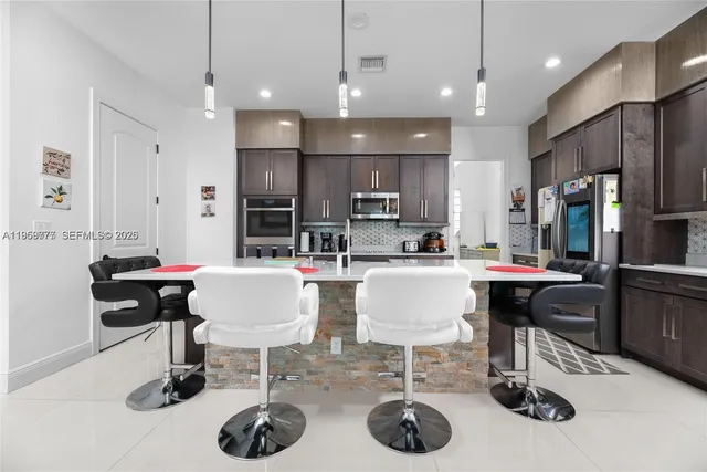 a kitchen with stainless steel appliances kitchen island granite countertop a table chairs and a refrigerator