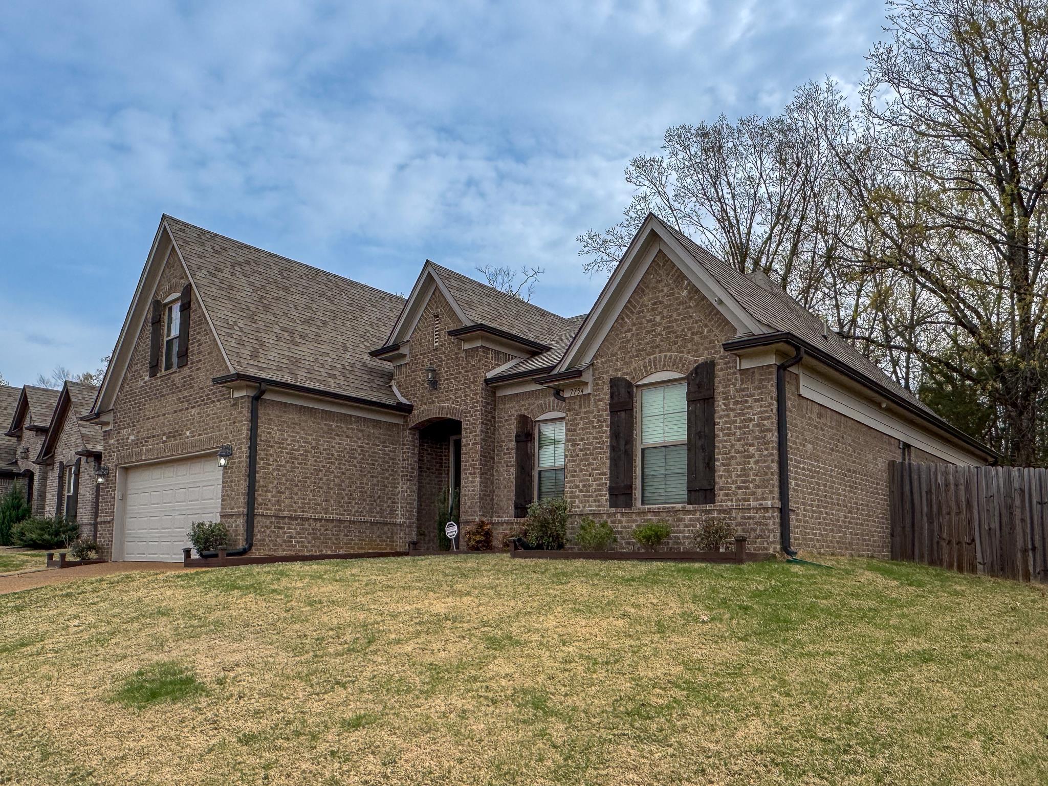 7754 Shadowcrest Road Memphis, TN 38125 - Photo 3 of 27 View of front of property featuring fence, brick siding, a front lawn, driveway, and a shingled roof