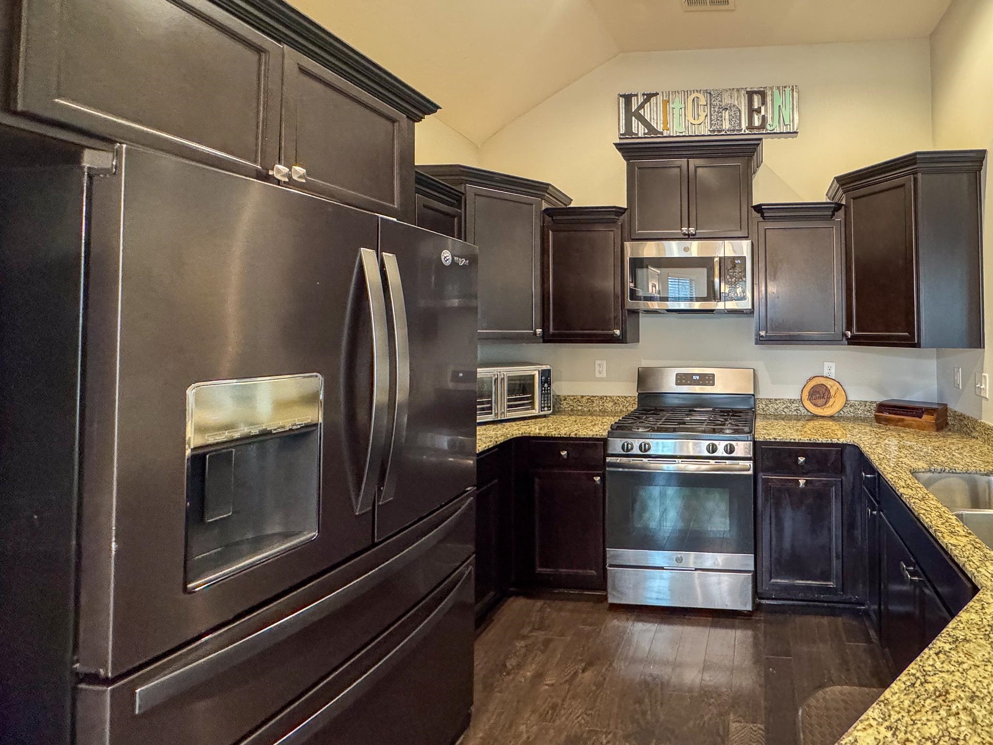 7754 Shadowcrest Road Memphis, TN 38125 - Photo 8 of 27 Kitchen with light stone countertops, stainless steel appliances, dark brown cabinets, dark wood finished floors, and vaulted ceiling
