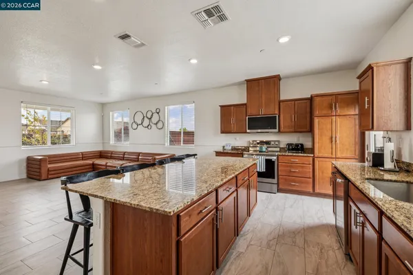 a kitchen with stainless steel appliances granite countertop a stove top oven a sink dishwasher a dining table and chairs with wooden floor