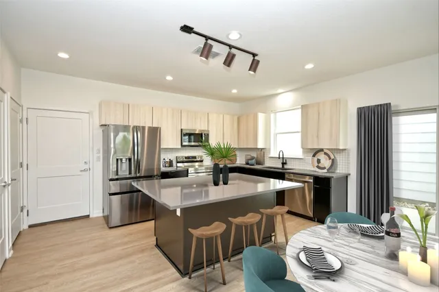 a kitchen with stainless steel appliances granite countertop a refrigerator a stove a sink a dining table and chairs with wooden floor