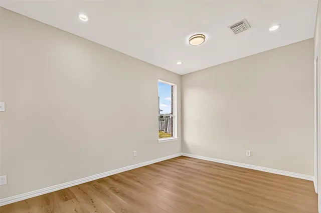 a view of an empty room with wooden floor and fan