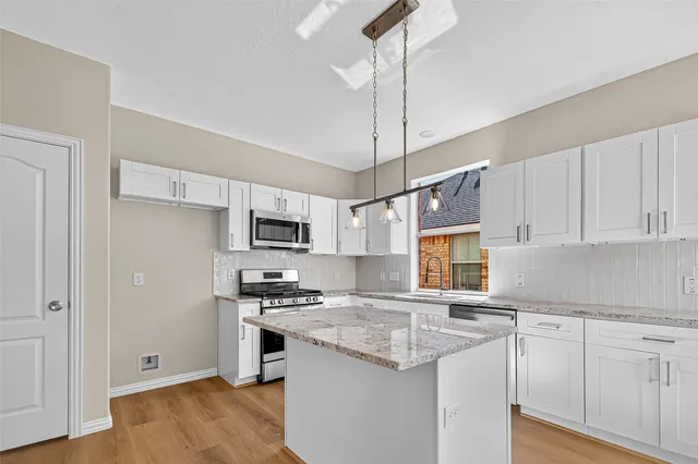 a kitchen with stainless steel appliances granite countertop a refrigerator a sink dishwasher a stove and white cabinets with wooden floor