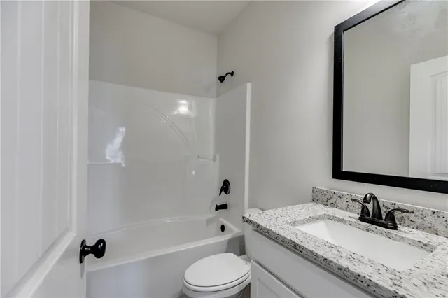 a bathroom with a granite countertop bathtub shower sink vanity mirror and toilet