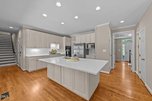 a large kitchen with kitchen island a sink dishwasher a refrigerator and white cabinets with wooden floor