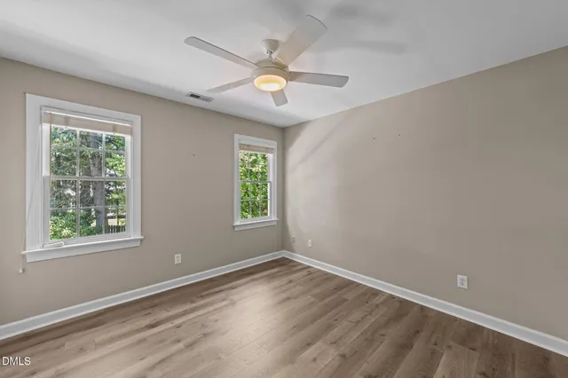 an empty room with wooden floor fan and windows