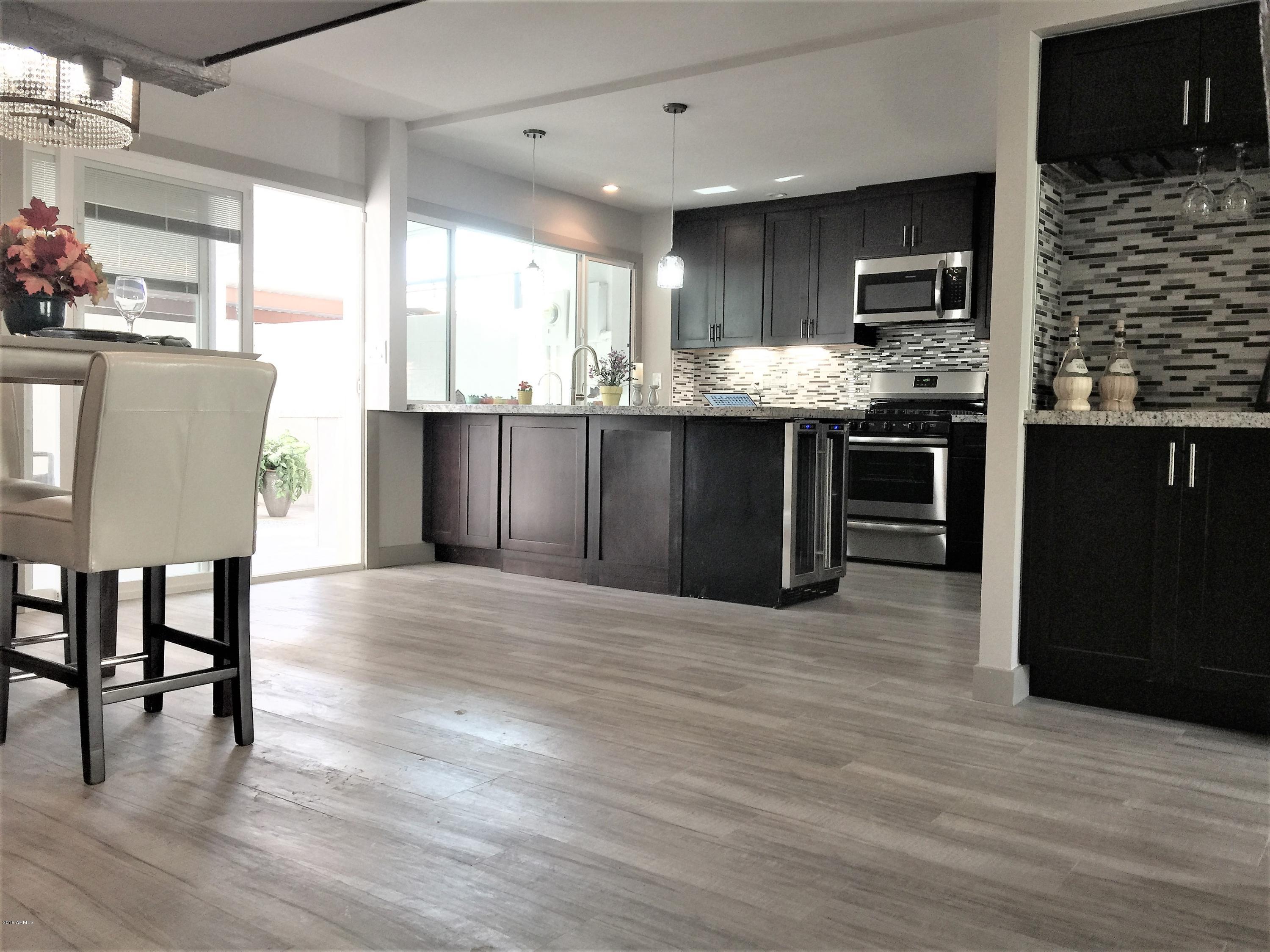 4221 North Miller Road Scottsdale, AZ 85251 - Photo 3 of 20 a kitchen with stainless steel appliances granite countertop a stove top oven a sink dishwasher a dining table and chairs with wooden floor