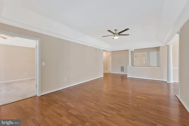 an empty room with wooden floor ceiling fan and windows