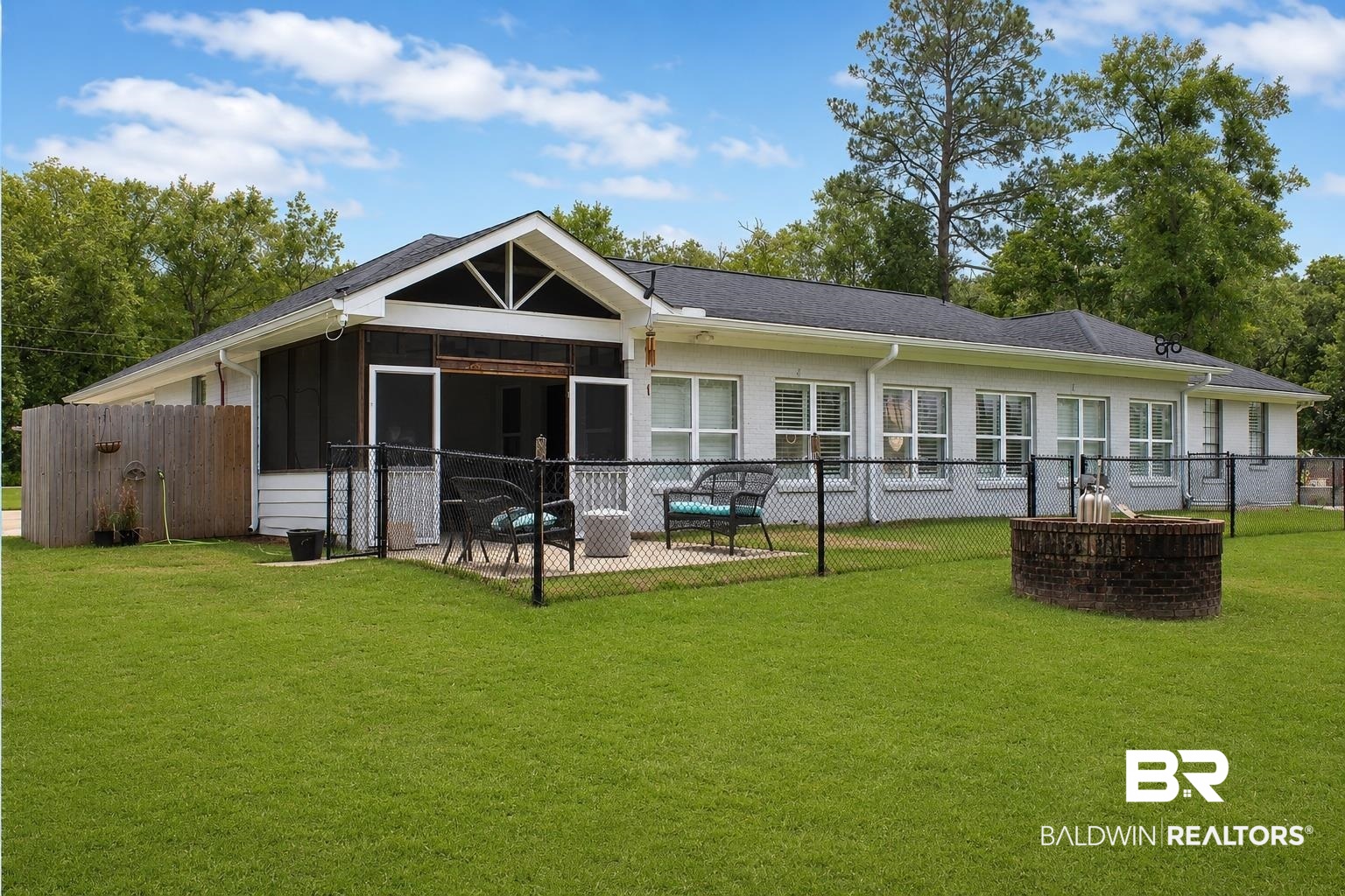 9825 Wolf Creek Ridge Elberta, AL 36530 - Photo 51 of 76 Expansive lawn area featuring a screened porch, chain-link fencing, a brick fire pit, and a light-colored exterior facade with multiple windows