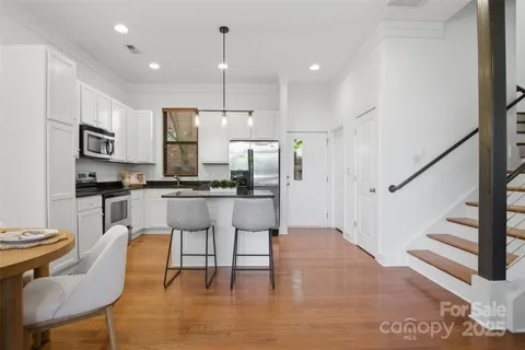 a kitchen with stainless steel appliances kitchen island granite countertop a refrigerator a stove a microwave oven a dining table and chairs with wooden floor