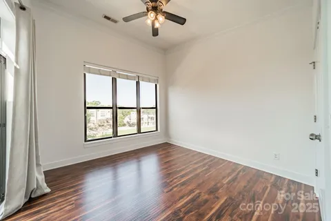 an empty room with wooden floor chandelier fan and windows