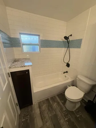 a bathroom with a granite countertop toilet a sink a mirror and bathtub