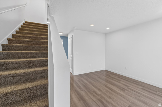 295 Spruce Way Santaquin, UT 84655 - Photo 3 of 32 Carpeted staircase featuring a white handrail, contrasting with a room showcasing wood-finish flooring, white baseboards, and recessed lighting