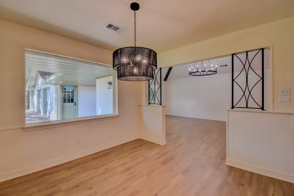 a view of a room with wooden floor chandeliers and kitchen view
