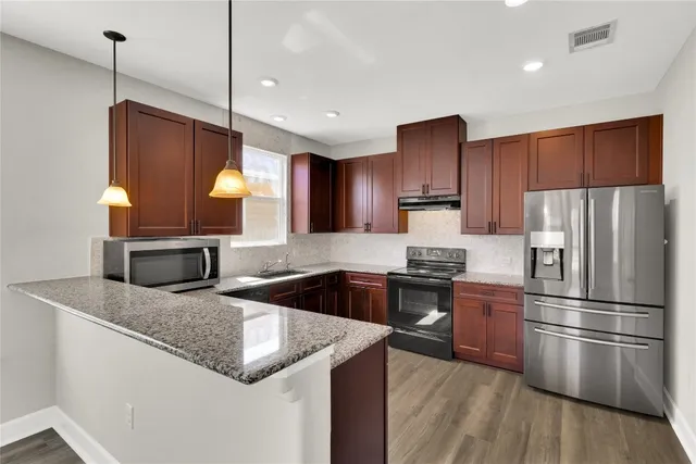 a kitchen with stainless steel appliances granite countertop a refrigerator a sink dishwasher a oven and a dining table with wooden floor