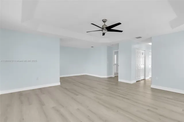 a view of an empty room with wooden floor and a ceiling fan