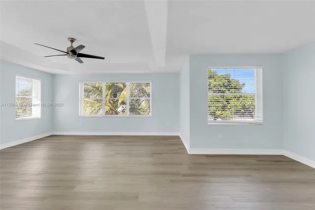 an empty room with wooden floor chandelier fan and windows