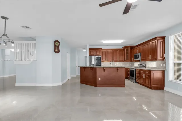 a living room with stainless steel appliances kitchen island granite countertop a refrigerator a stove a oven a sink with island and chairs in it
