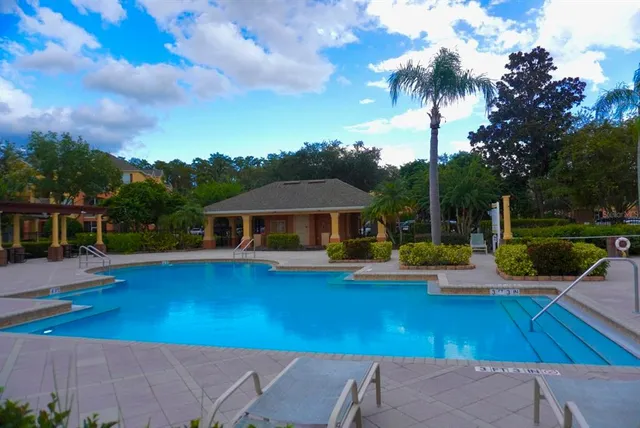 a view of pool with lawn chairs under an umbrella