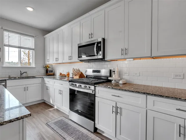 a kitchen with granite countertop white cabinets white stainless steel appliances a sink and a window