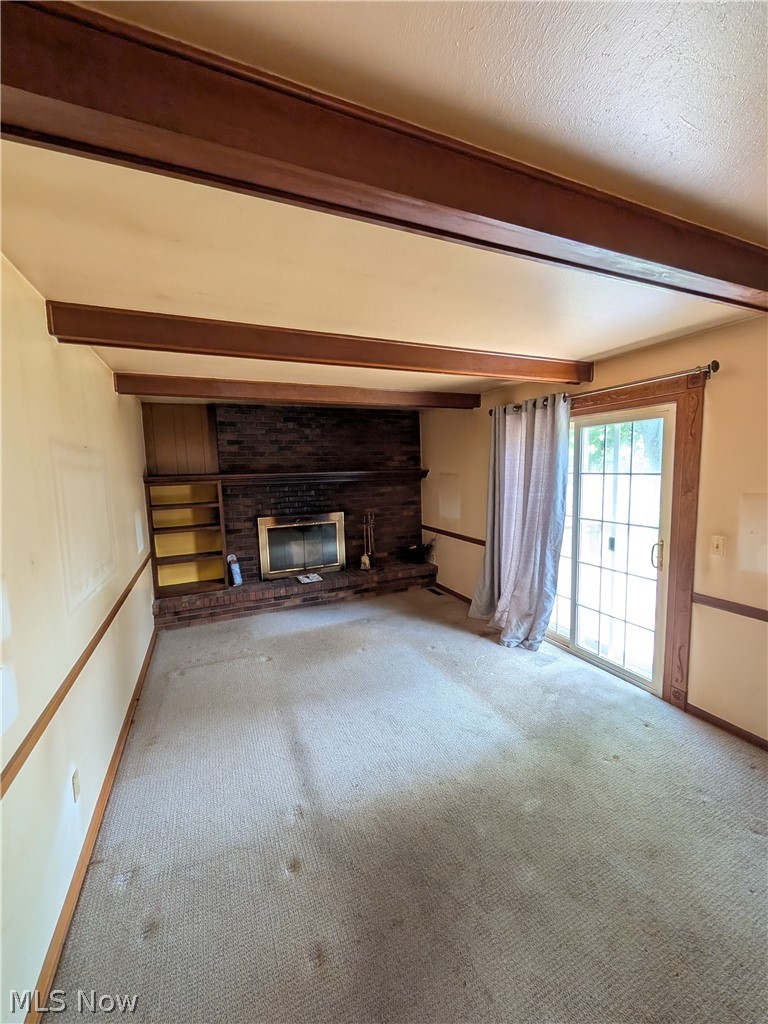 1161 Gulf Road Elyria, OH 44035 - Photo 15 of 34 Living space featuring exposed wood ceiling beams, a brick fireplace with an integrated mantel, built-in shelving, and a sliding glass door