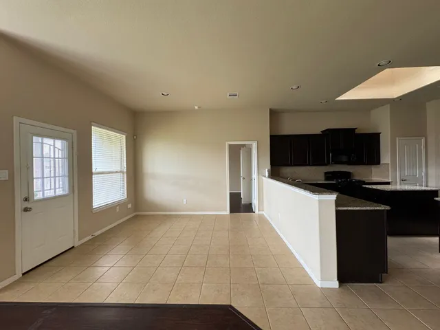 a view of an empty room with kitchen and window