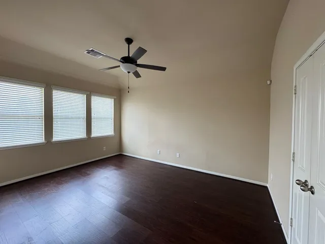 an empty room with wooden floor fan and windows