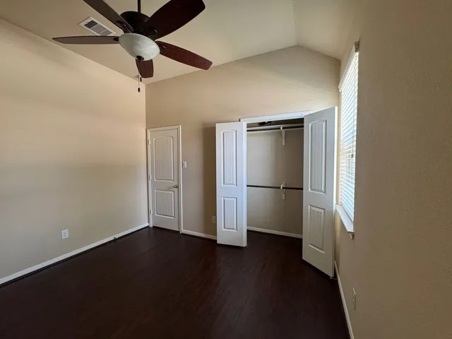 an empty room with wooden floor a ceiling fan and kitchen view