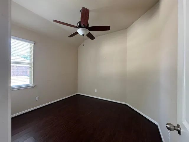 a view of a small space with wooden floor a ceiling fan and windows