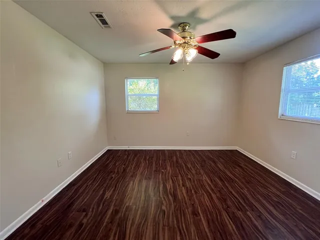 a view of an empty room with wooden floor and a chandelier fan