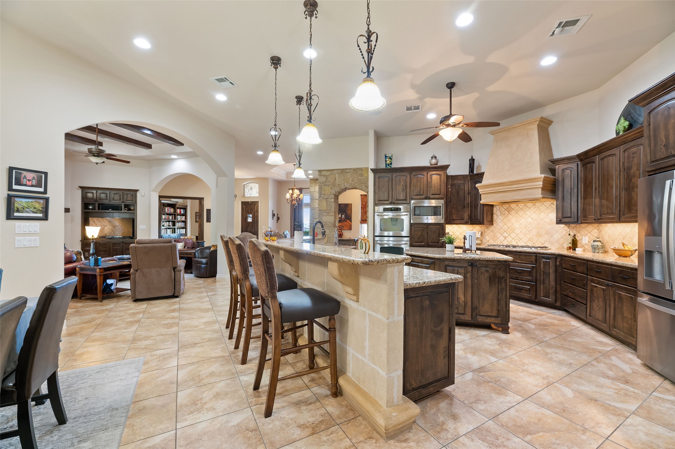 109 Ranchers Club Lane Driftwood, TX 78619 - Photo 9 of 19 Kitchen with ceiling fan, decorative light fixtures, dark brown cabinets, a kitchen breakfast bar, and arched walkways