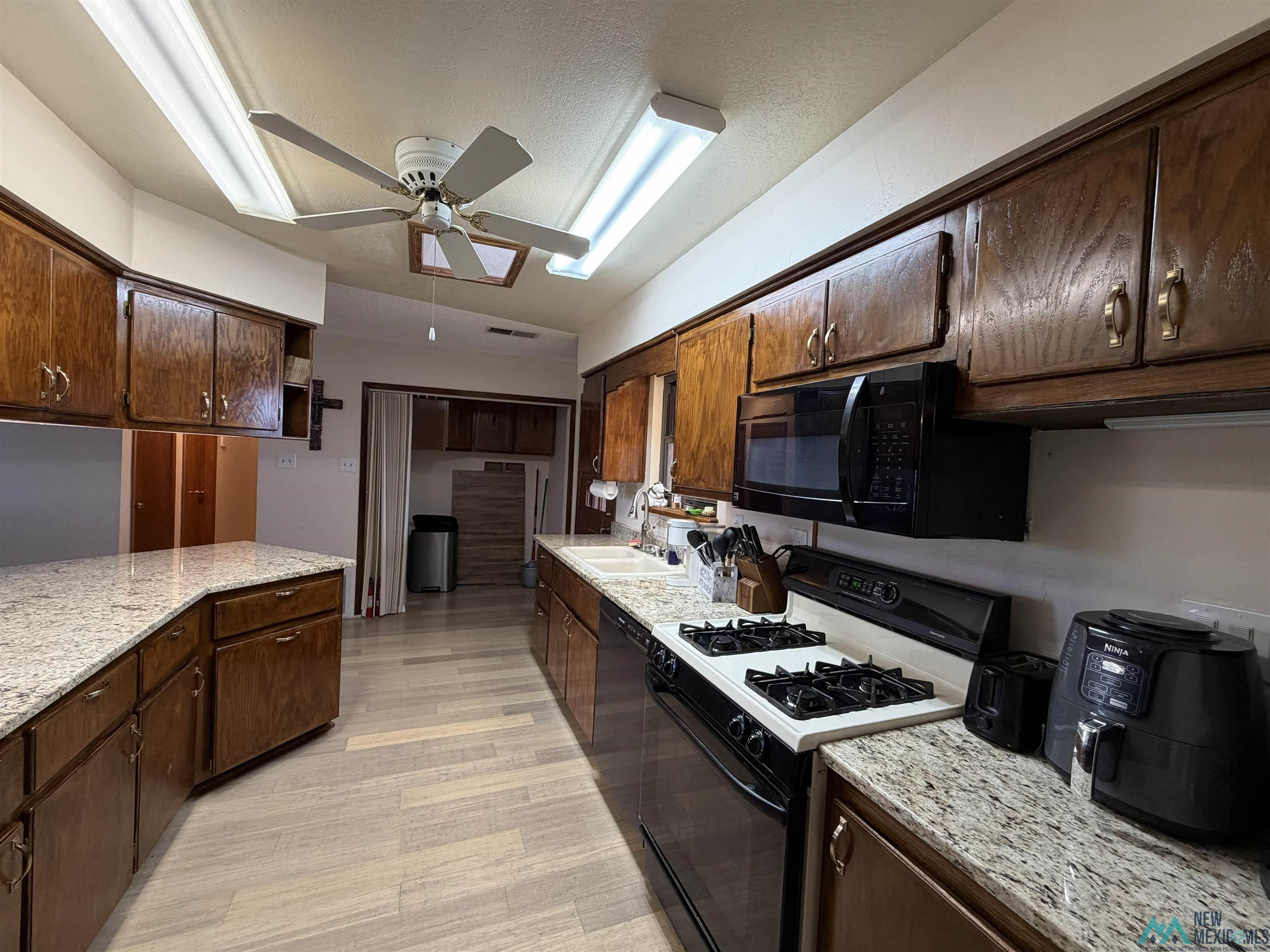 2001 East Derrick Road Carlsbad, NM 88220 - Photo 47 of 84 Kitchen featuring black appliances, dark wood finish cabinetry, ceiling fan, light stone counters, and light wood-style floors