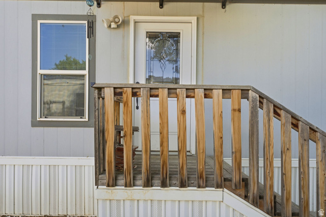 2875 North Hill Field Road, Unit 62 Layton, UT 84041 - Photo 7 of 34 Front entry featuring wood-plank railing and steps, a white paneled door with decorative glass inlay, and light gray vertical siding