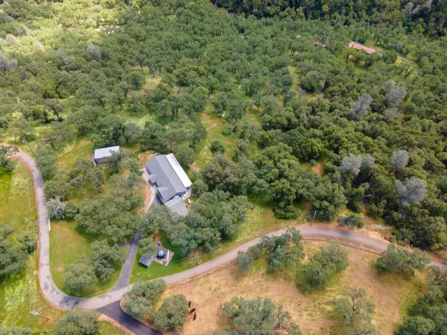 an aerial view of residential house with outdoor space and trees all around
