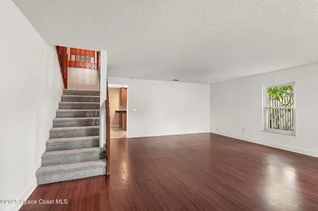 a view of an empty room with wooden floor and stairs