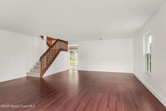 a view of an empty room with wooden floor and stairs