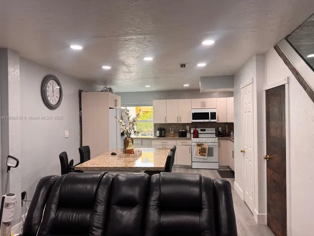 a living room with stainless steel appliances furniture a clock and a view of kitchen