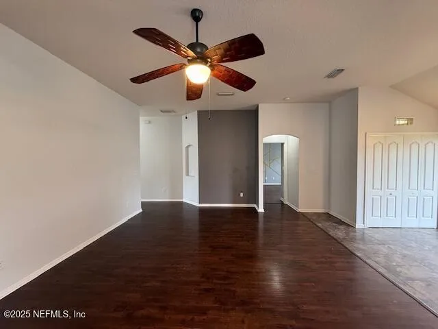 a view of an empty room with wooden floor and a ceiling fan